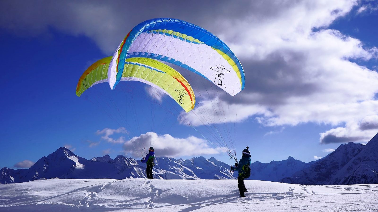 Two speedflying wings being ground-handled on a snowy ridge